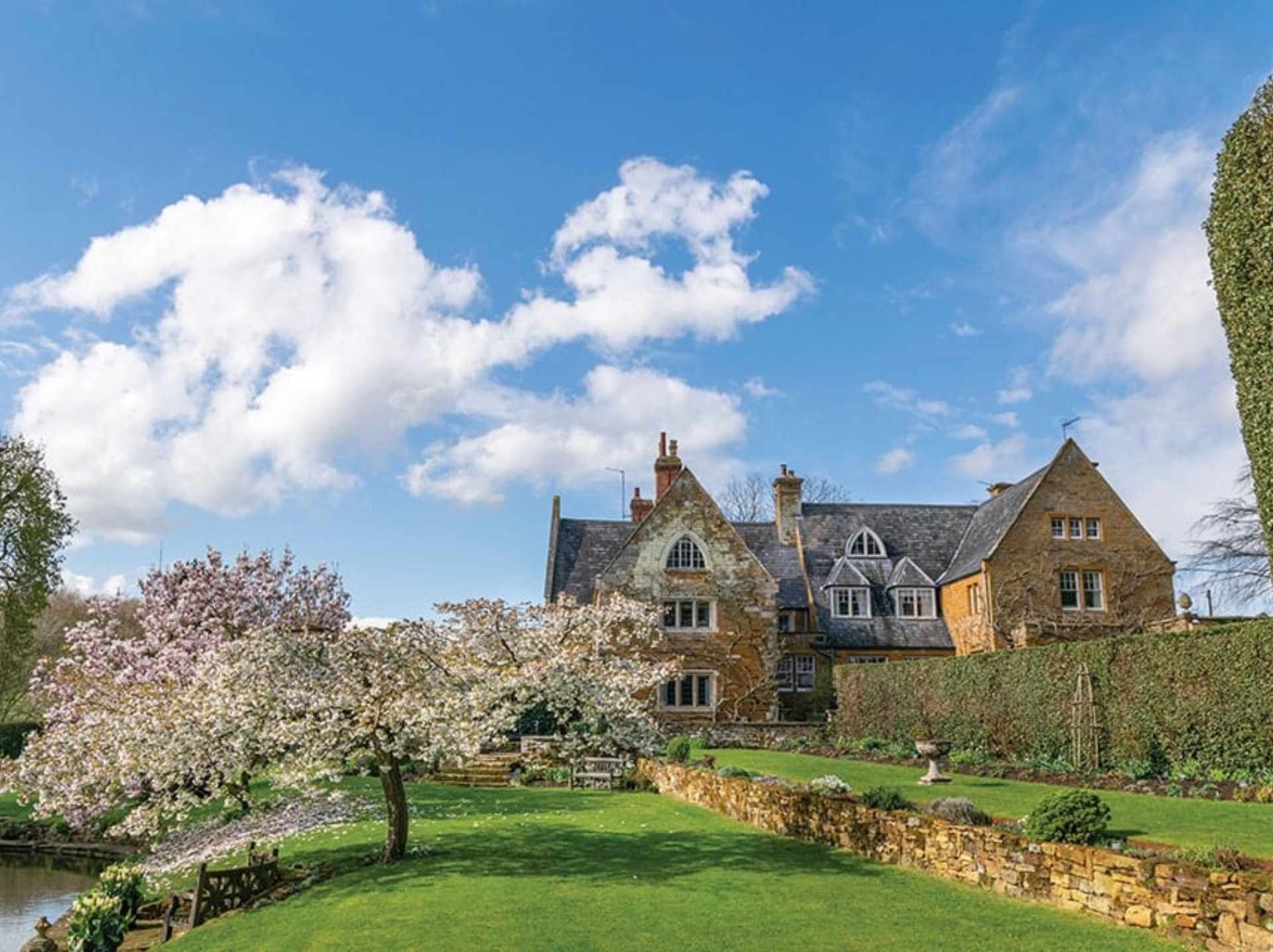 colour photo of Coton Manor Garden with a blossom tree on the left and exterior of a building on the right