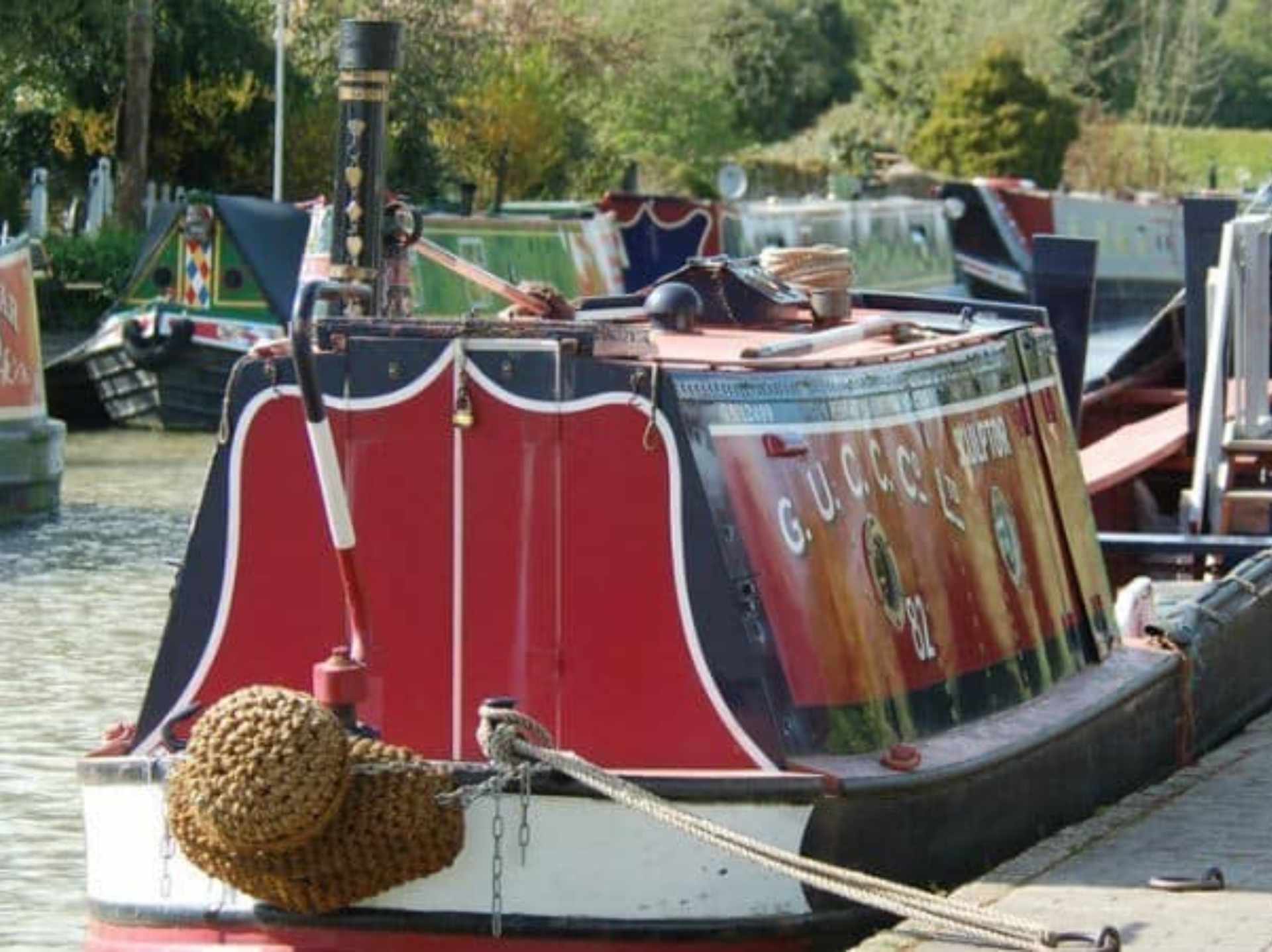 colour photo of a canal boat in the canal, from the front, which is painted red and navy